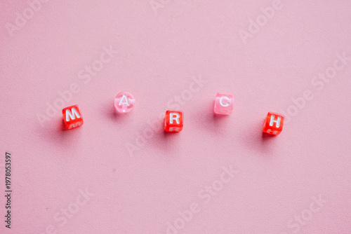 March Month Spelled with Red and Pink Alphabet Beads on Pink Background