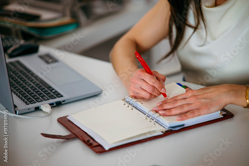 Woman writing notes in planner by laptop
