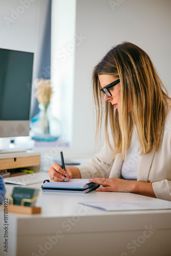 Professional woman writing notes on notebook at office desk