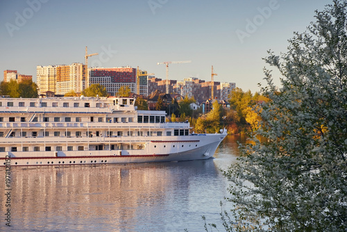 Fotografie White motor ship on the river, against the backdrop of buildings under construct