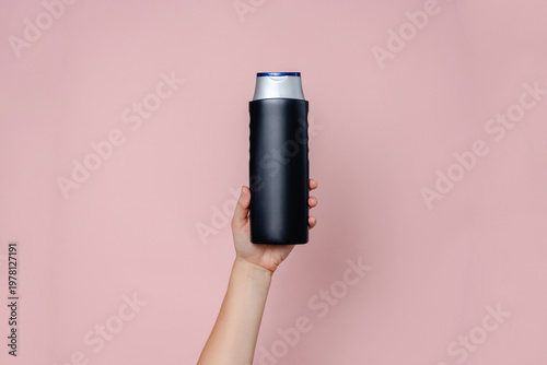Woman's hand holding shampoo bottle on the solid pink background. Cosmetics product package, your brand, spa. Space for text
