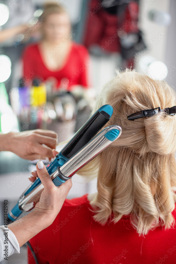 Fototapeta premium Hairdresser styling blonde hair with a curling iron in a salon setting