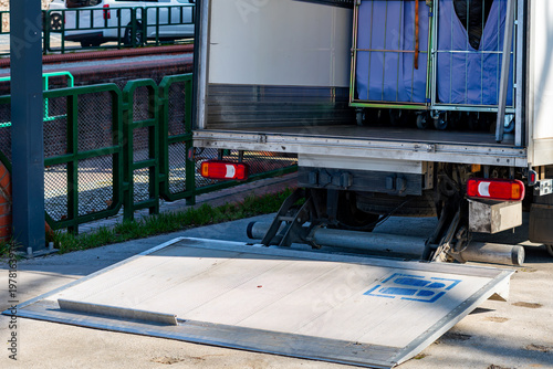 Foto Delivery truck with hydraulic tail lift lowered for unloading goods, metal roll cage container inside the vehicle, city logistics, freight transport and courier delivery service