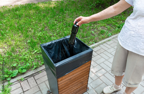 A person disposes of a bottle in a public trash can.
