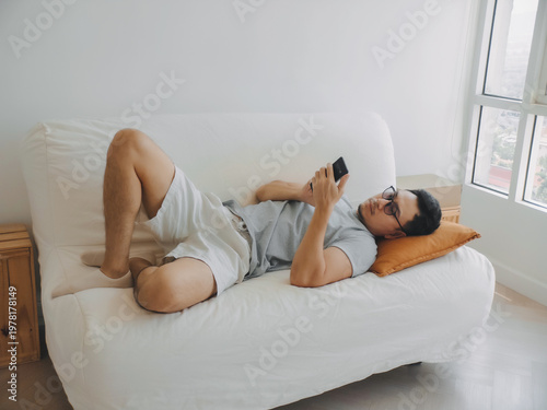 Asian man focus on the phone while relaxed on the sofa.