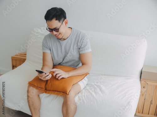Asian man sitting comfortably on couch composing digital message