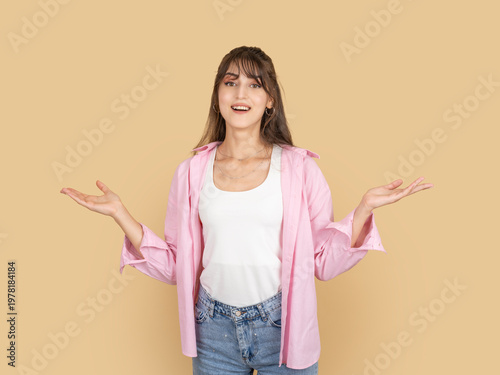 Foto Smiling caucasian woman shrugging with open hands, expressing uncertainty or indifference concept idea image, wearing pink shirt and denim, isolated on beige background with copy space