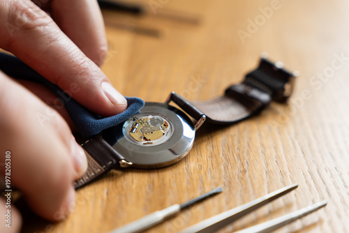 Fotografia Hand is polishing the back of a wristwatch with a leather strap on a wooden tabl