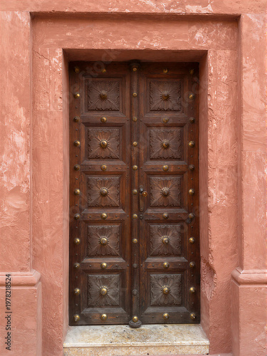 Intricately carved wooden Zanzibar door with brass spikes in a coral stone wall