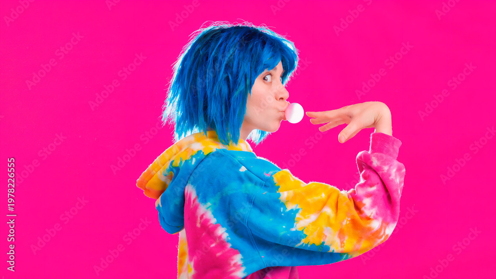 Fototapeta premium Profile of a young person with bright blue hair blowing a bubblegum bubble against a vibrant pink background