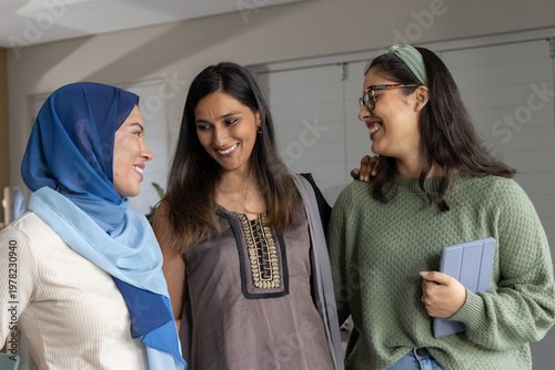 Obraz na płótnie Diverse female friends smiling and chatting in lounge wearing blue hijab and hol