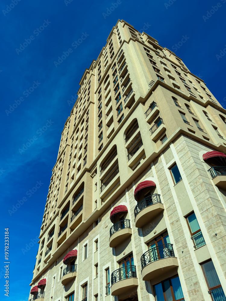 Fototapeta premium Tall building reaches for the blue sky in a city with clear weather and bright sunlight, showcasing its architecture and design from a low angle view