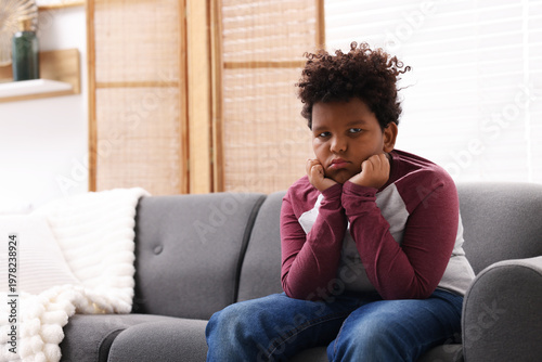 Fotografie Portrait of resentful little boy sitting on sofa at home