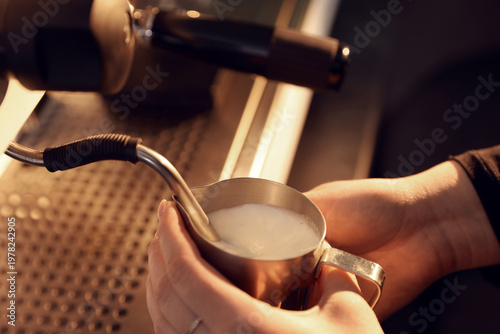 Photos Barista frothing milk in metal pitcher with coffee machine wand in cafe, closeup