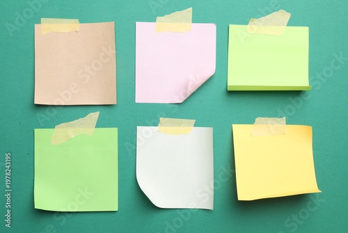 Blank paper notes with adhesive tape on green background, top view