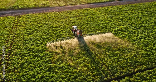 Aerial view of tractor spraying pesticides on a green field