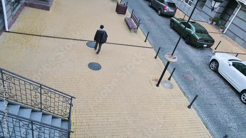 Urban Street Scene with a Person Walking on Yellow Brick Pavement and Parked Modern Cars - High Angle View