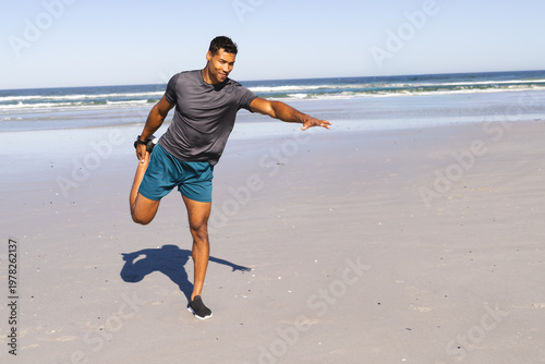 Valokuva Man stretching and balancing on leg at sandy beach with teal shorts, running sho
