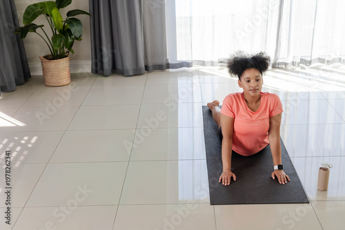 Fotografie African American woman wearing coral top doing backbend on black yoga mat at hom