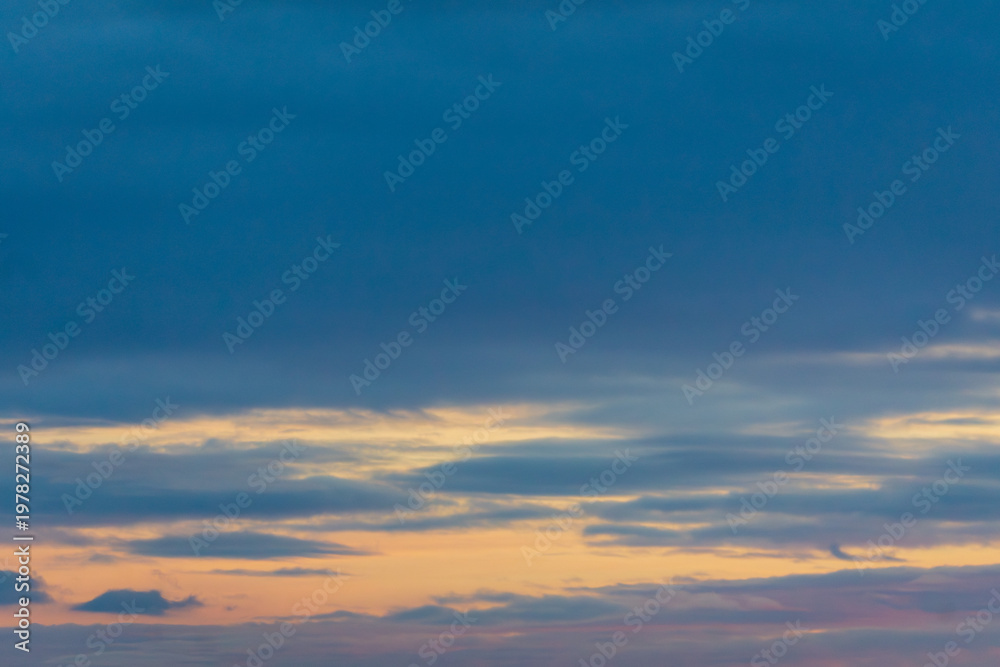 Fototapeta premium Soft blue and yellow sunset sky with layered clouds