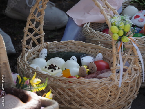 Wicker Easter basket decorated with flowers and filled with eggs and traditional food outdoors