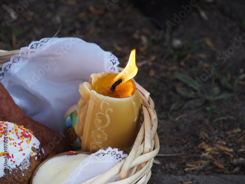 Selective focus on a burning candle flame in a basket filled with Easter delicacies.
