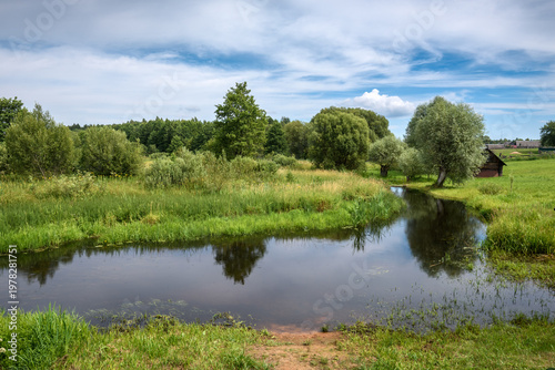 Horizontal Landscape Of River Bend With Wooden House And Tree Reflections Under Cloudy Sky