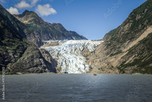 Massive Chilkat Glacier in Alaska towering above tranquil fjord waters with a small canoe in the foreground