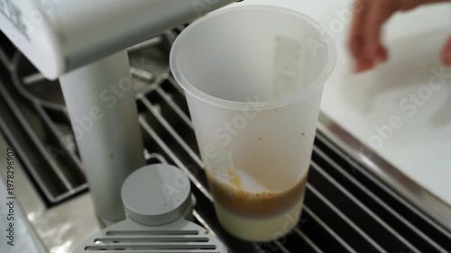rich espresso being poured into a transparent cup of cold milk and ice cubes to create an iced coffee latte. Professional barista preparation in a clean, minimalist cafe setting.