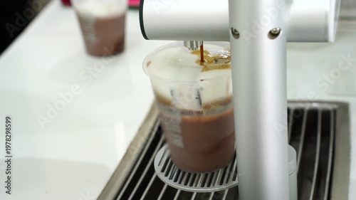 rich espresso being poured into a transparent cup of cold milk and ice cubes to create an iced coffee latte. Professional barista preparation in a clean, minimalist cafe setting.