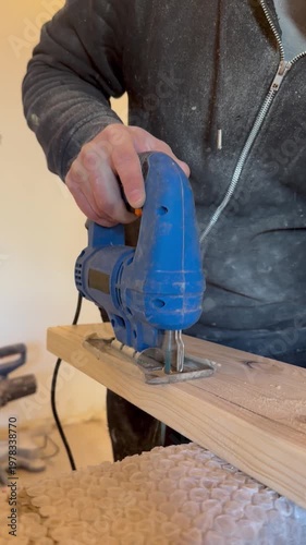 Close-up of a craftsman’s hand using a jigsaw to cut and shape wood. Detailed woodworking process in a workshop setting.