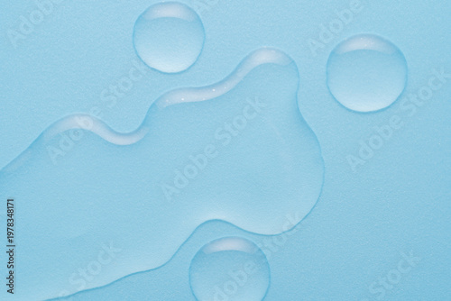 Clear moisturizing gel drops on light blue background. Aqua cosmetic liquid texture swatch.