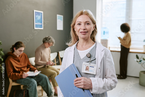 Fotografie Portrait of middle aged Caucasian female doctor standing in clinic waiting room, holding patient files and smiling