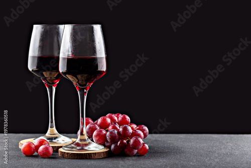 Grapes wine. Two wine glasses filled with rich red wine positioned next to cluster of fresh grapes on dark surface creating sophisticated and inviting composition for wine enthusiasts and connoisseurs