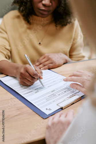 Konstfotografi Vertical shot of Black woman signing medical form during consultation while clinician pointing at document