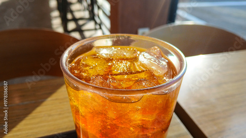 close up of iced tea or cold brew coffee with ice cubes in a glass on a table with warm sunlight and lens flare at an outdoor cafe