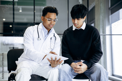 Medical doctor wearing a lab coat and stethoscope consulting a young male patient, discussing diagnosis and treatment