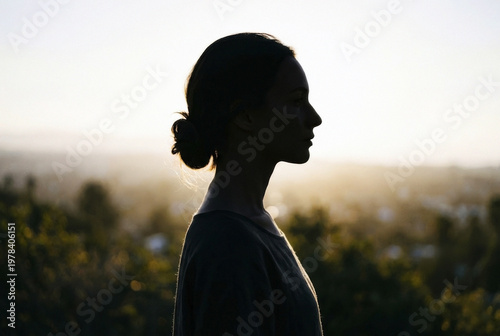 Side profile of woman with bun looking out over blurry city view at sunset