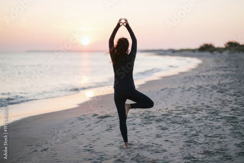Young woman practicing yoga tree pose on a sandy beach during a beautiful golden hour sunset with calm ocean waves