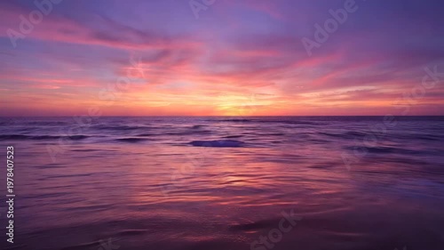 Beautiful orange sunset over the calm sea with soft waves and purple clouds in the sky