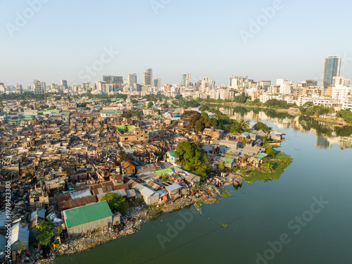 Aerial view of a sharp contrast between the dense, haphazard settlements along the riverbank and the modern skyline in the distance, Dhaka, Dhaka Division, Bangladesh.
