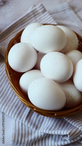 Fresh white eggs rest in a woven basket on a soft striped cloth, showcasing the beauty of natural ingredients in a cozy kitchen setting