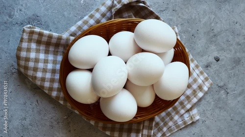 A beautiful assortment of white eggs fills a woven basket, elegantly placed on a checkered cloth in a rustic kitchen atmosphere.