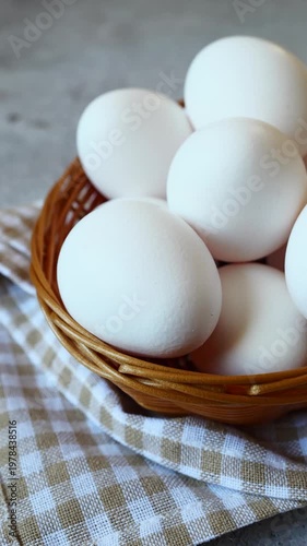 Gathering fresh white eggs in a rustic woven basket on a textured stone surface with a cozy checkered cloth underneath