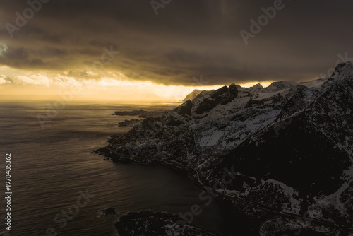 Aerial view of dramatic cliffs meeting the moody sea under a brooding sky, Reinebringen, Nordland, Norway.