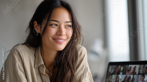 Smiling young woman in a cozy room, glancing aside beside a laptop during a video call.