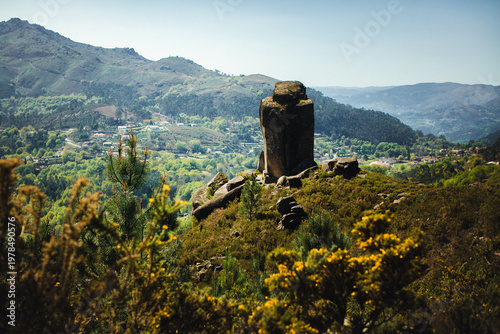 Rock formation on a hill overlooking a green valley with villages and mountains in Portugal, scenic countryside landscape.