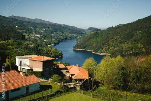 River valley landscape with village houses and green hills in Portugal under clear sky, scenic countryside view.