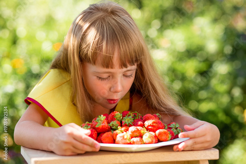 Canvastavla A pretty blonde girl in a yellow dress enjoys the fragrance of strawberries
