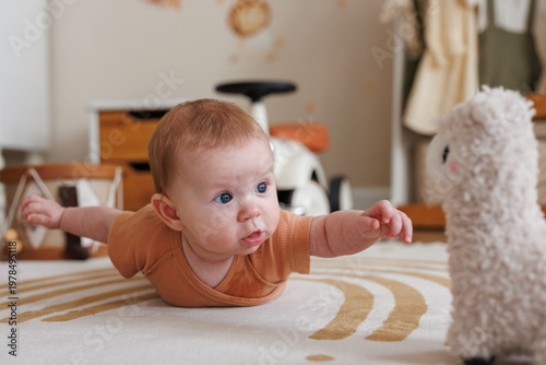 An infant reaching out towards a fluffy llama toy while lying on a rug in a sunlit nursery